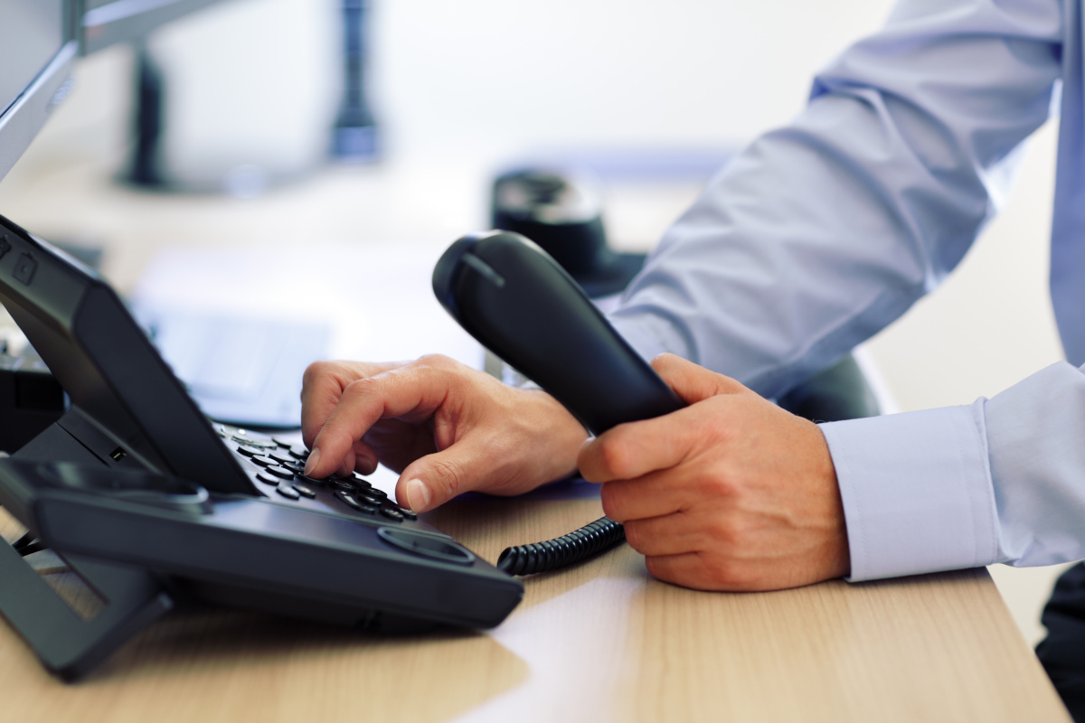 A close up of a mand holding a phone receiver in one hand and dialing on its keypad with the other