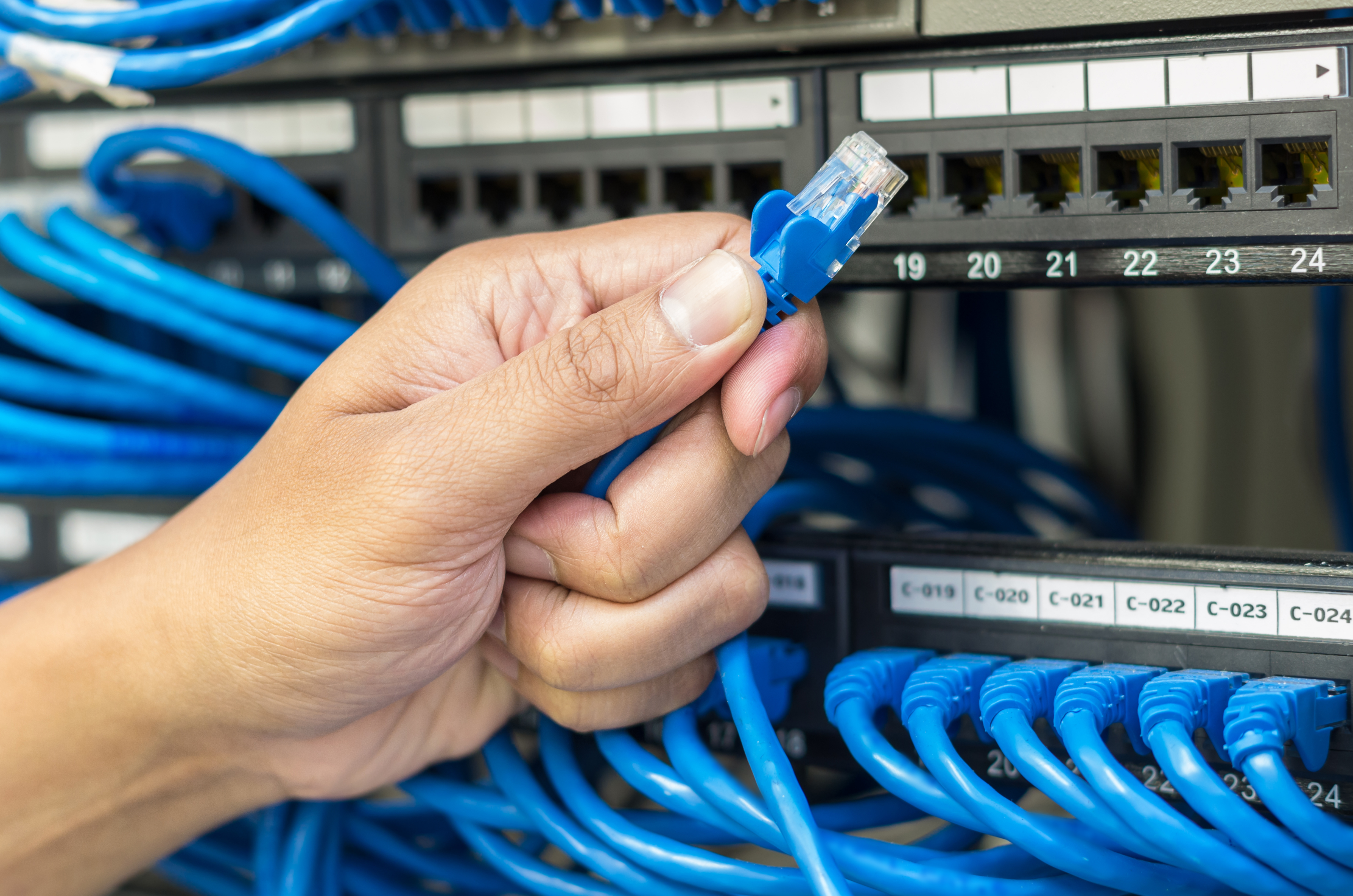 Hand Holding Network Cable Connection to Router and Switch Hub in Server Room